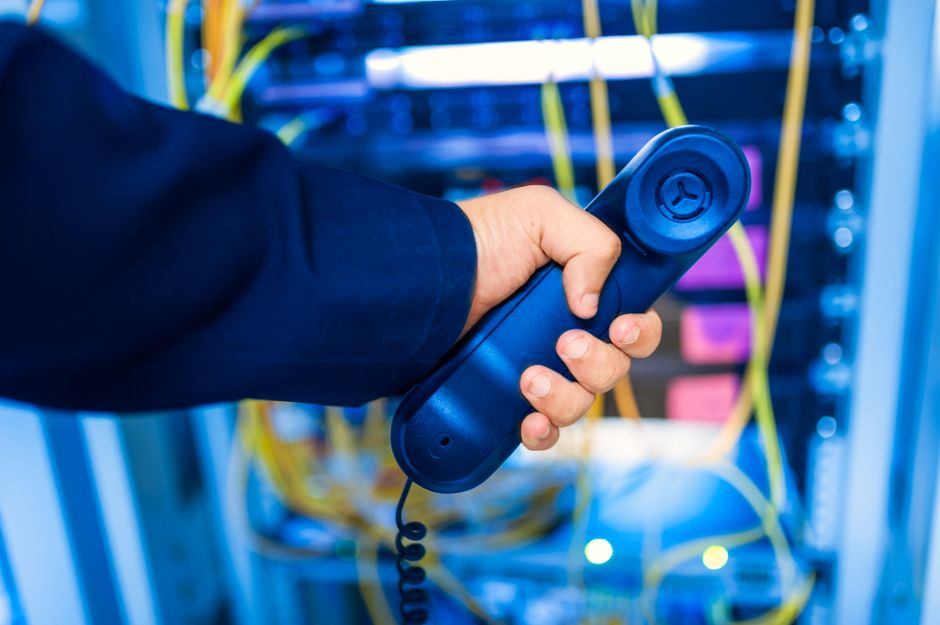 Close-up de uma mão segurando um fone de telefone em uma sala de servidores, enfatizando a tecnologia.