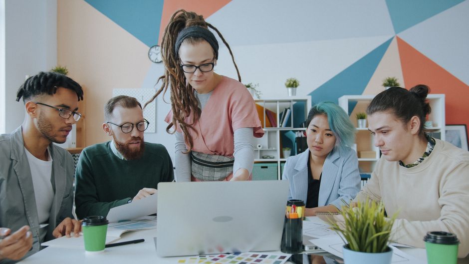 Uma equipe diversificada de adultos colabora em um escritório moderno, analisando documentos e usando um laptop.