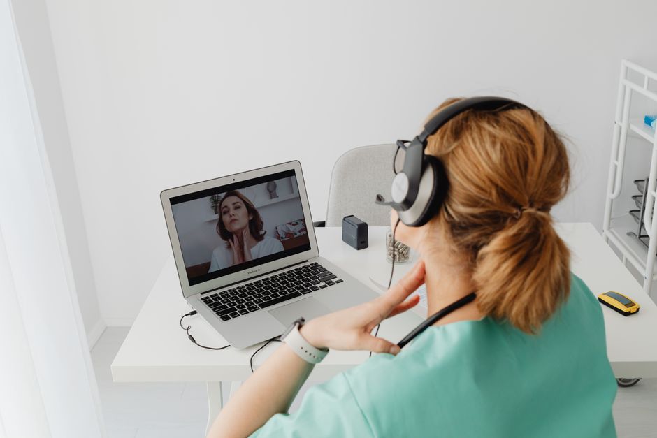 Mulher em roupas médicas participando de uma sessão de telemedicina usando um laptop em casa.
