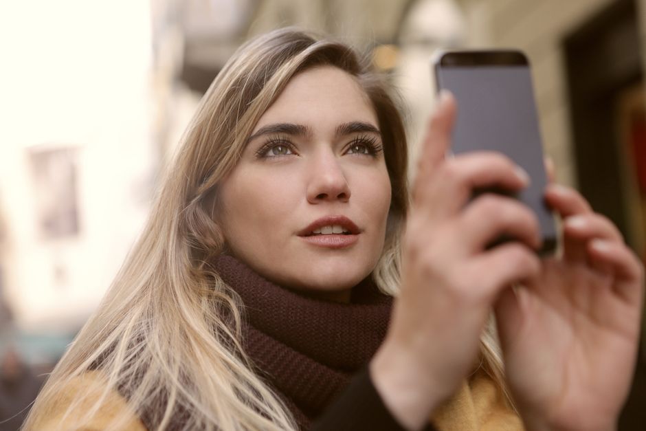 Retrato de uma jovem tirando fotos com seu smartphone em um ambiente urbano.
