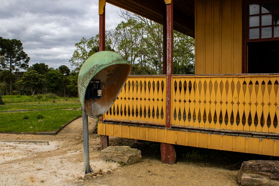 Cabine telefônica antiga ao lado de uma casa rústica de madeira em Alfredo Wagner, Brasil.