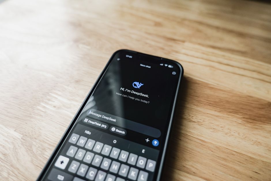 Um smartphone exibindo uma interface de bate-papo com IA, DeepSeek, em uma mesa de madeira.