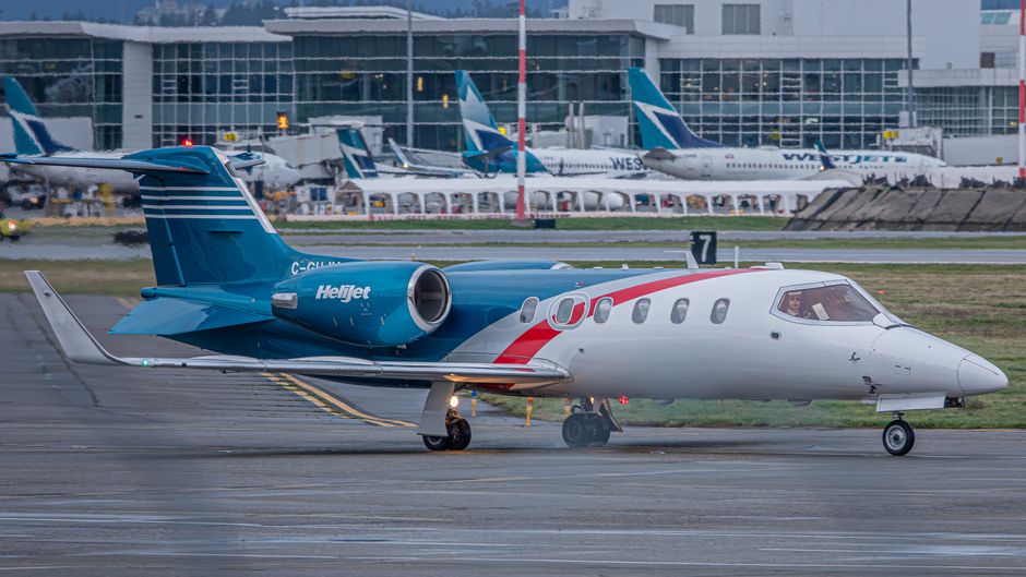 Uma aeronave Helijet posicionada na pista do aeroporto com o terminal ao fundo.