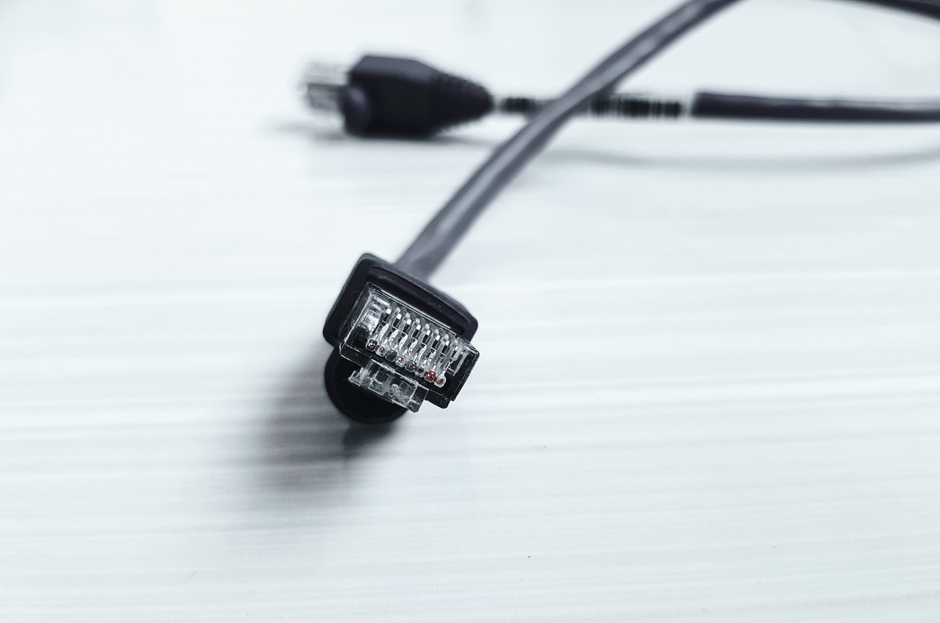 Imagem detalhada de um cabo ethernet preto com conector RJ-45 sobre uma superfície branca.