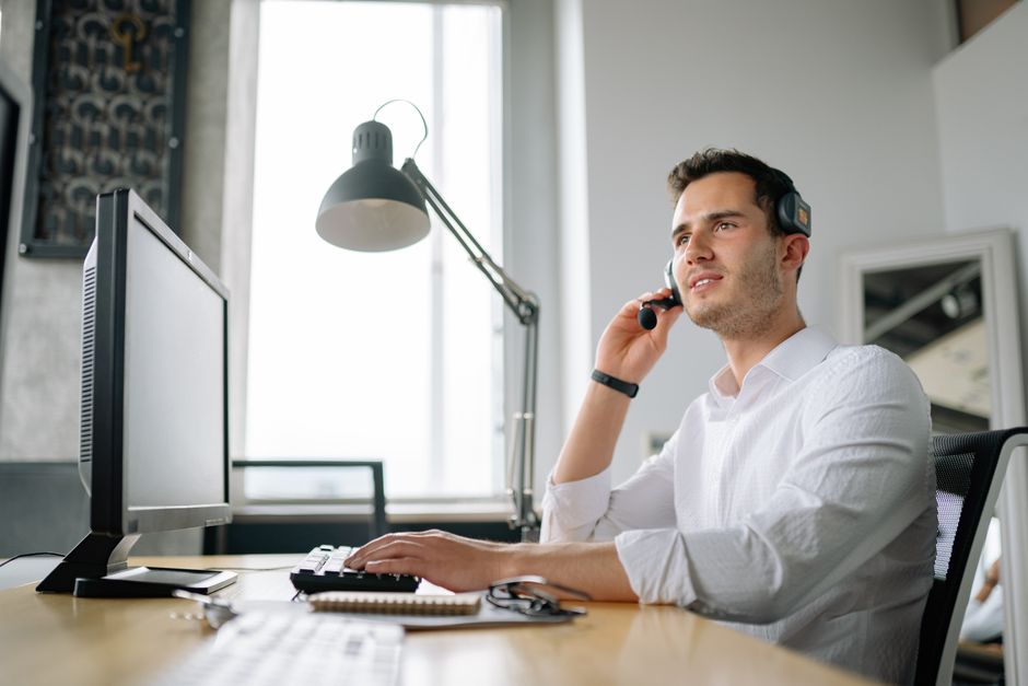 Agente de call center masculino com fone de ouvido trabalhando na mesa, oferecendo excelente atendimento ao cliente.