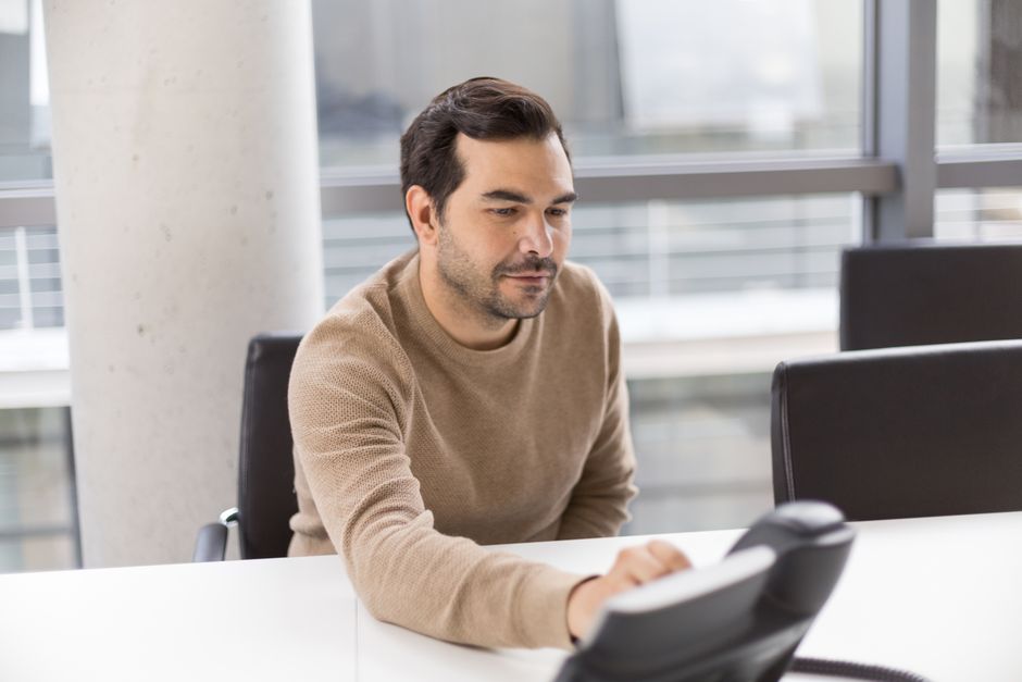 Um homem em um escritório moderno trabalhando com um telefone de mesa, mostrando um ambiente profissional de negócios.