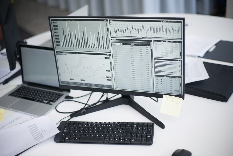 Um espaço de trabalho profissional com computadores e gráficos analíticos em um monitor, simbolizando o ambiente de negócios moderno.