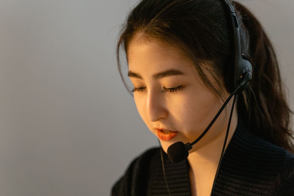Mulher jovem e focada com headset trabalhando no suporte ao cliente, falando atentamente.
