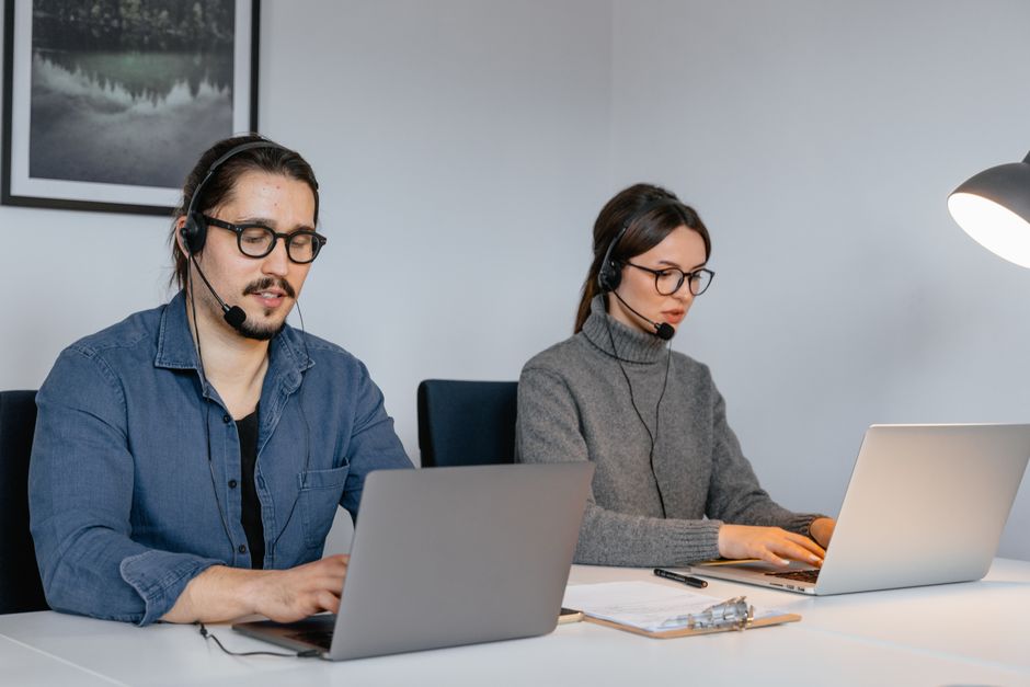 Dois agentes de call center focados trabalhando em laptops com headsets em um ambiente de escritório.