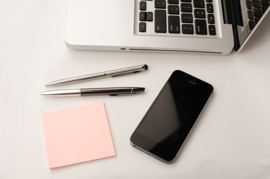Espaço de trabalho limpo e moderno com um laptop, smartphone, canetas e notas adesivas.